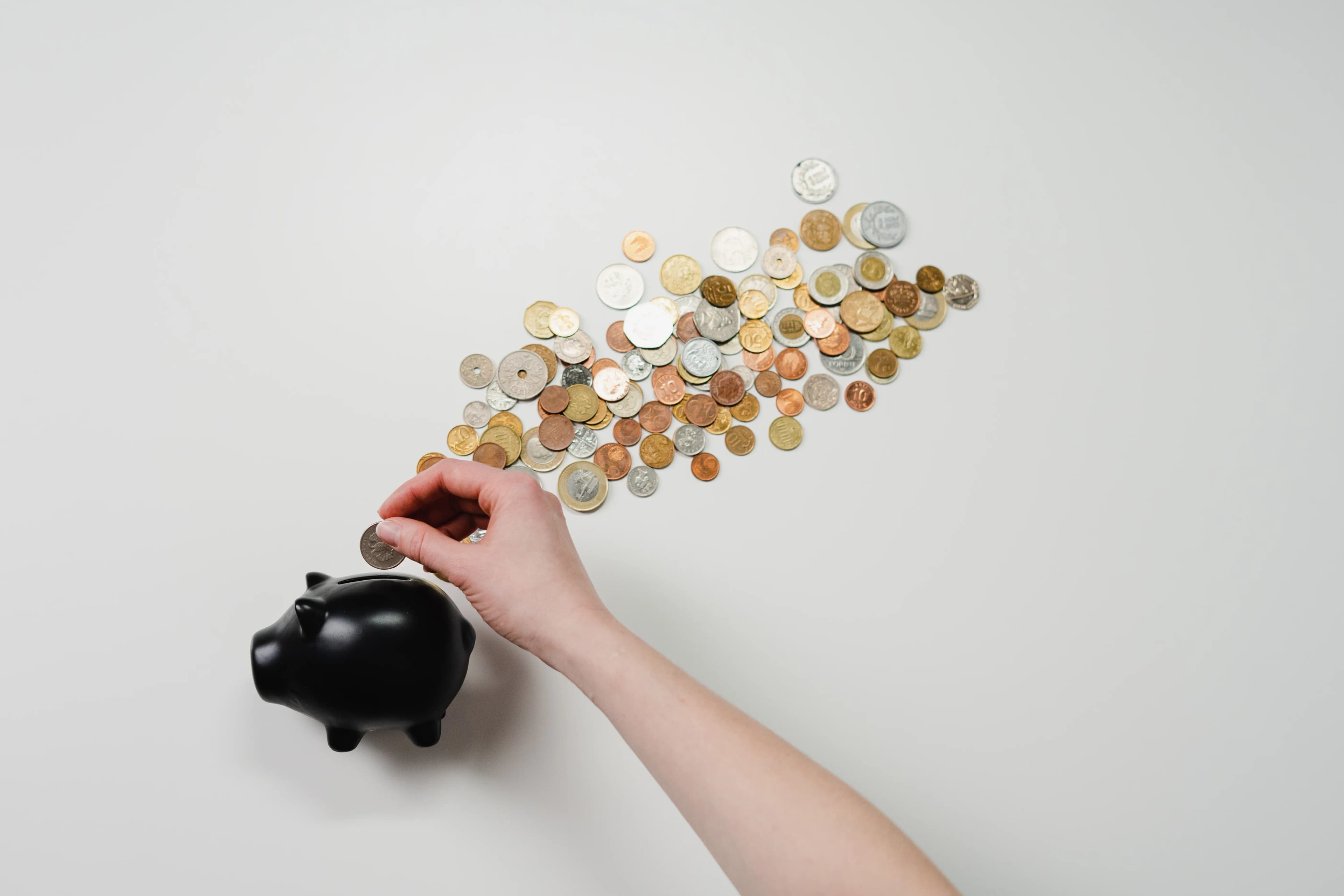 A hand putting a coin into a piggy bank surrounded by coins, representing 401k retirement savings