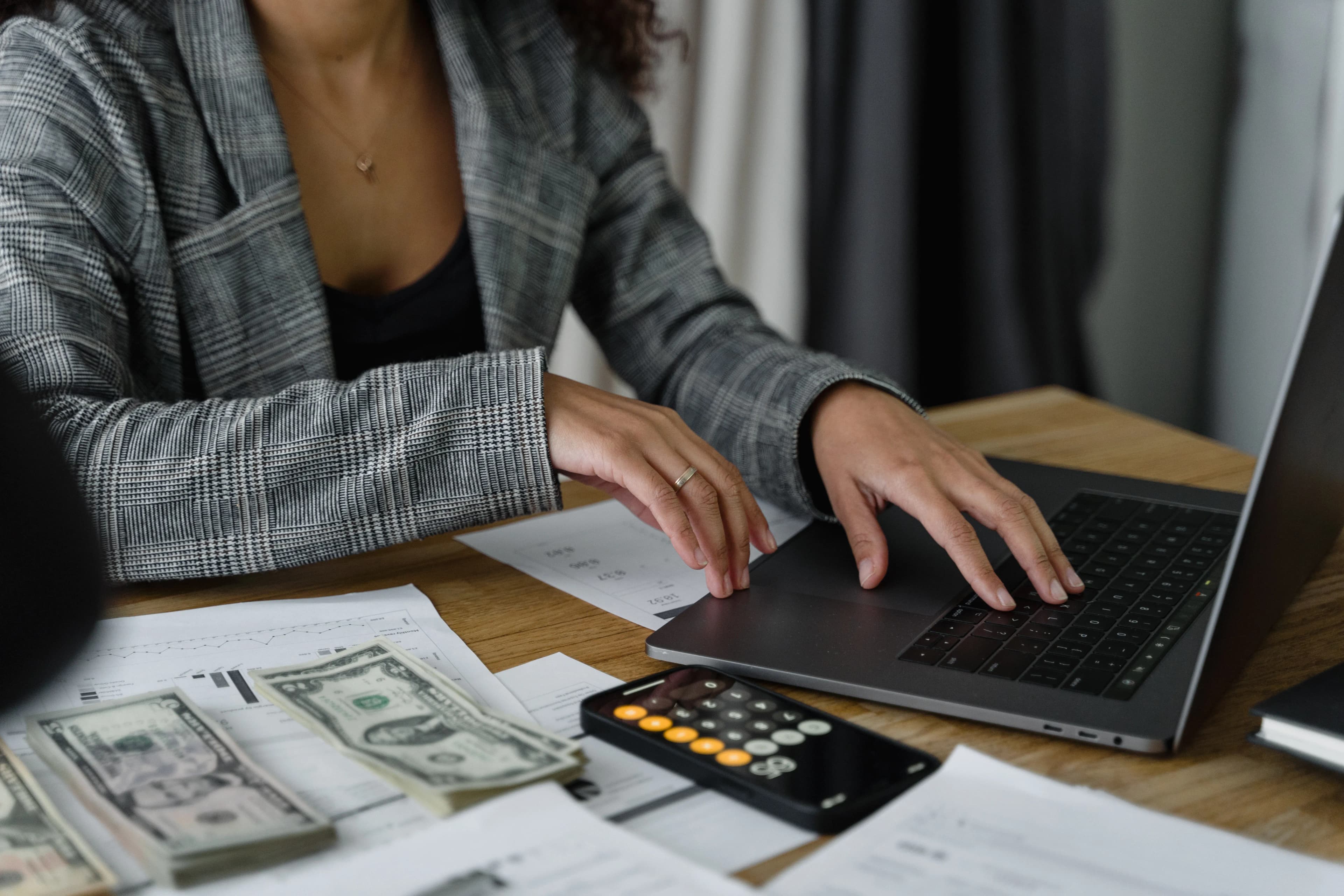 A person working on a laptop with cash and a calculator, representing capital gains tax