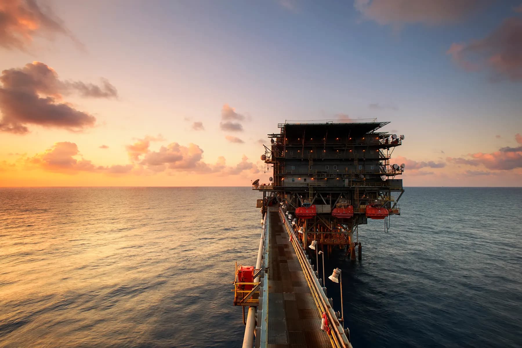 An offshore oil rig at sunset, representing crude oil surging past 100 dollars
