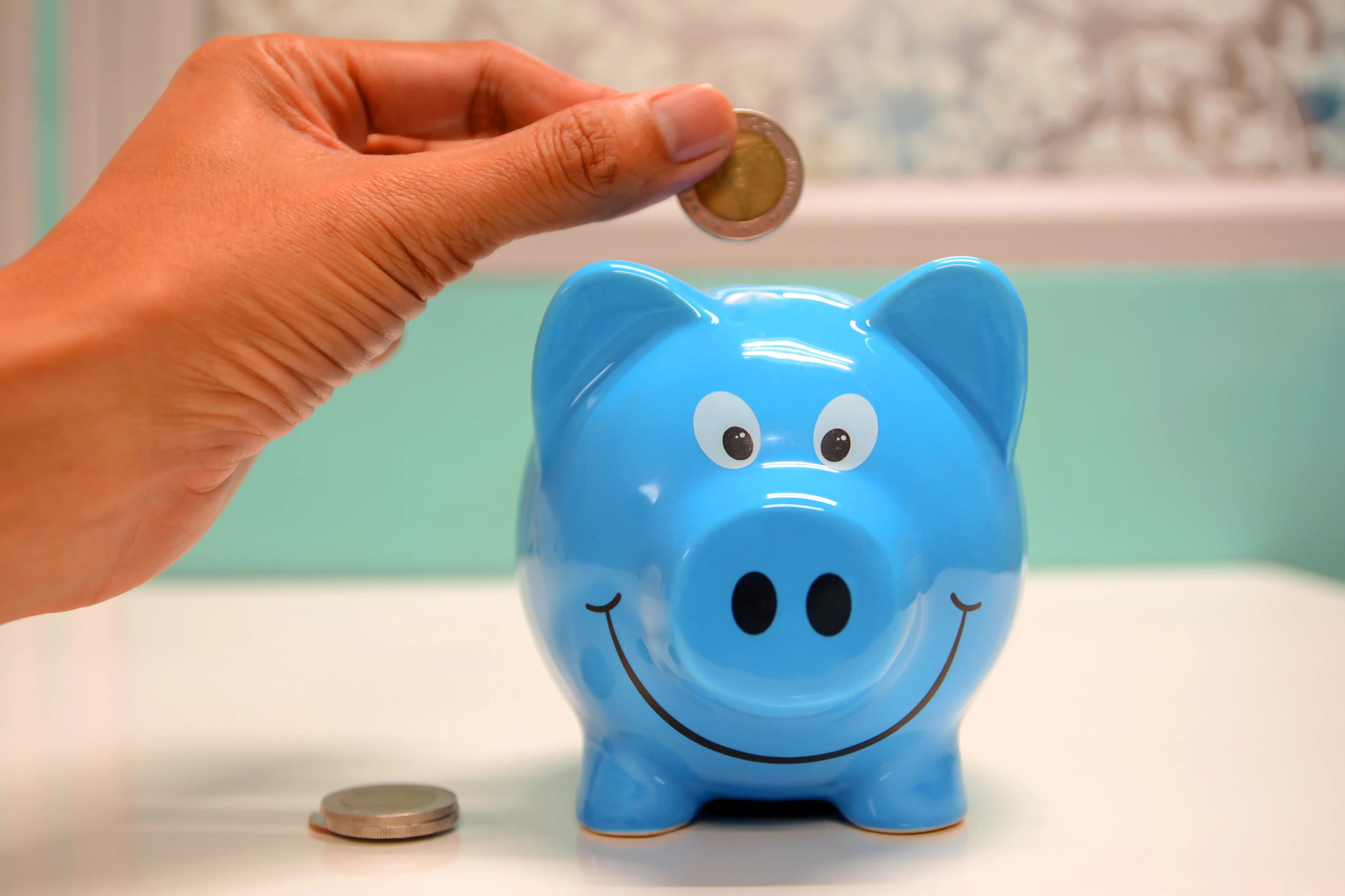A hand dropping a coin into a smiling piggy bank, representing October 2026 dividend payments