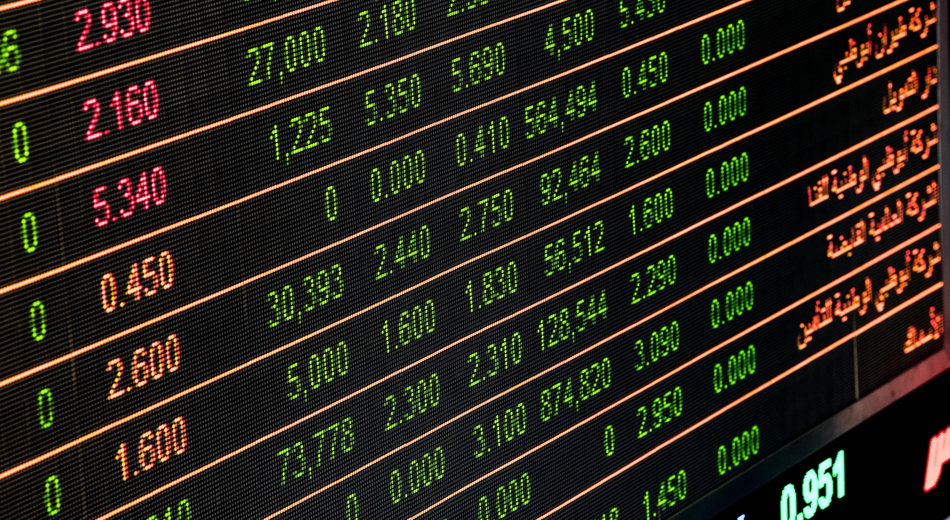 A stock market ticker board showing green and red numbers, representing US market volatility