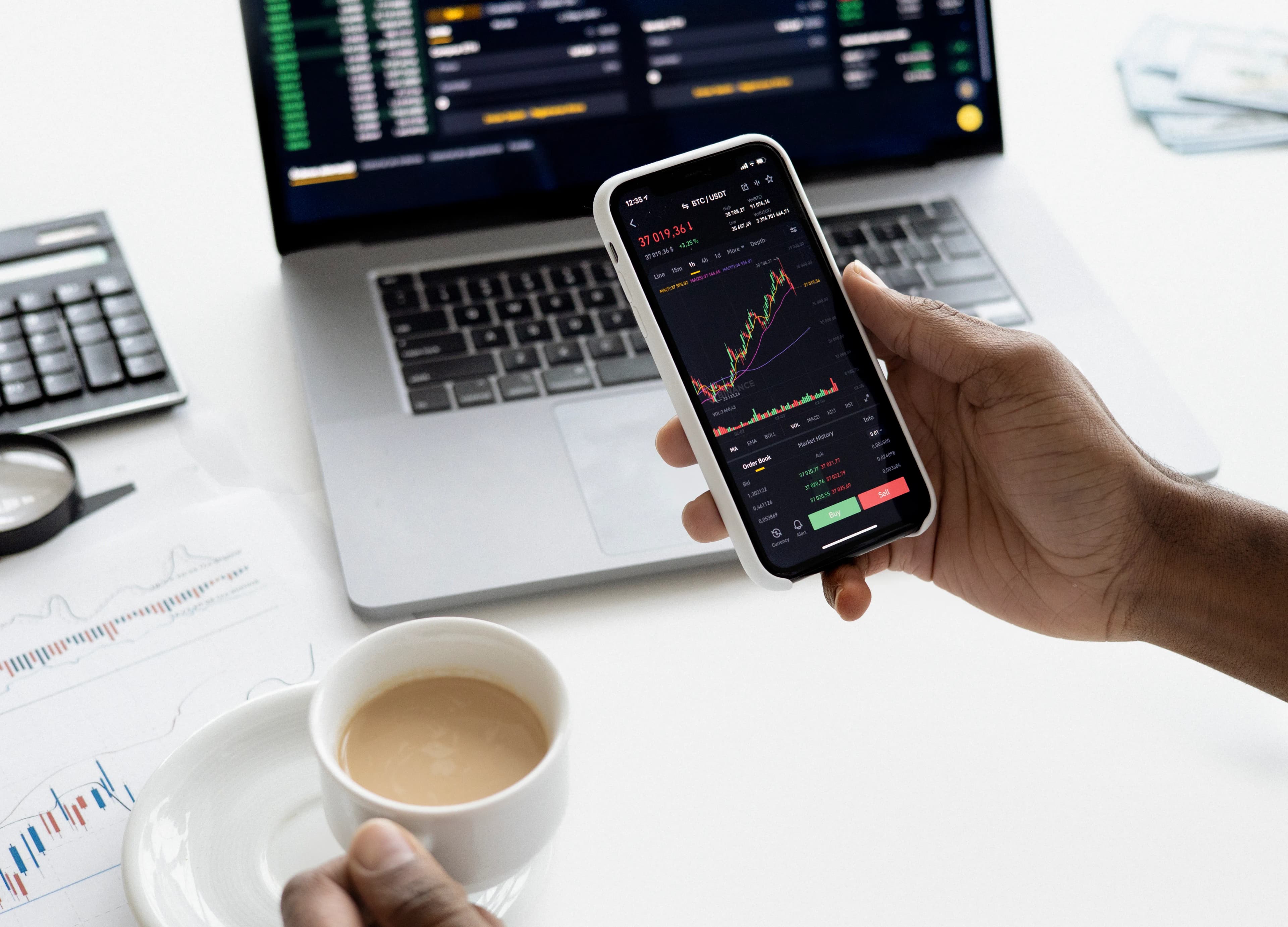 A person checking a stock trading app next to a laptop and coffee, representing index ETF investing